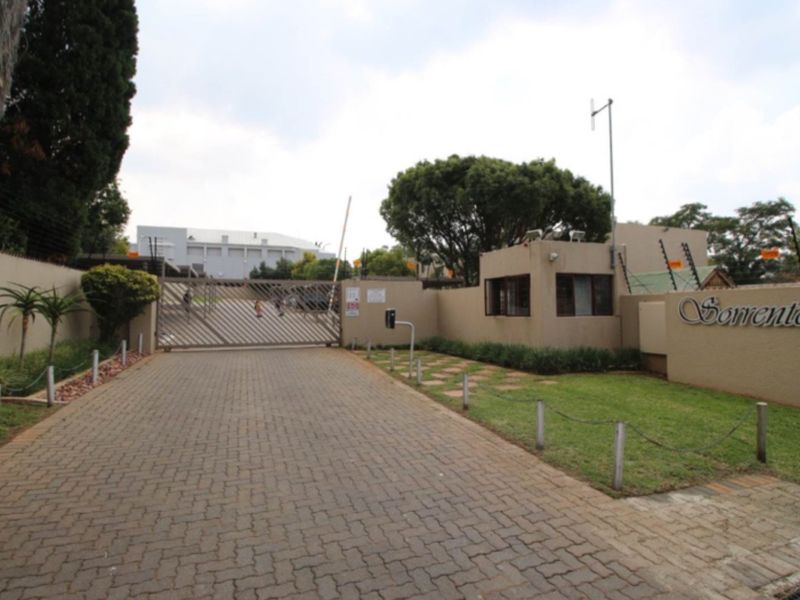 Entrance to the Sorrento complex featuring a paved driveway, security gate, and guard house with perimeter fencing.