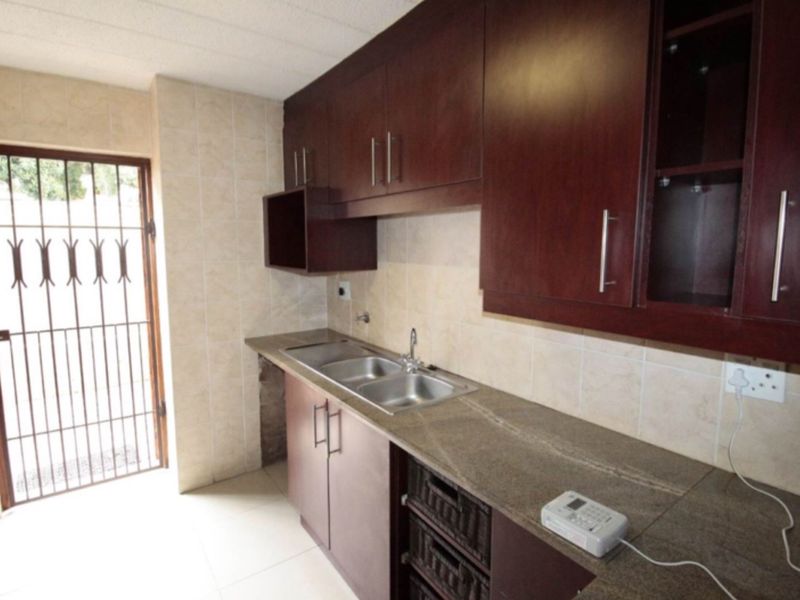 A functional kitchen featuring dark wood cabinetry, stone-look countertops, a double stainless steel sink, and a security gate leading to the exterior.