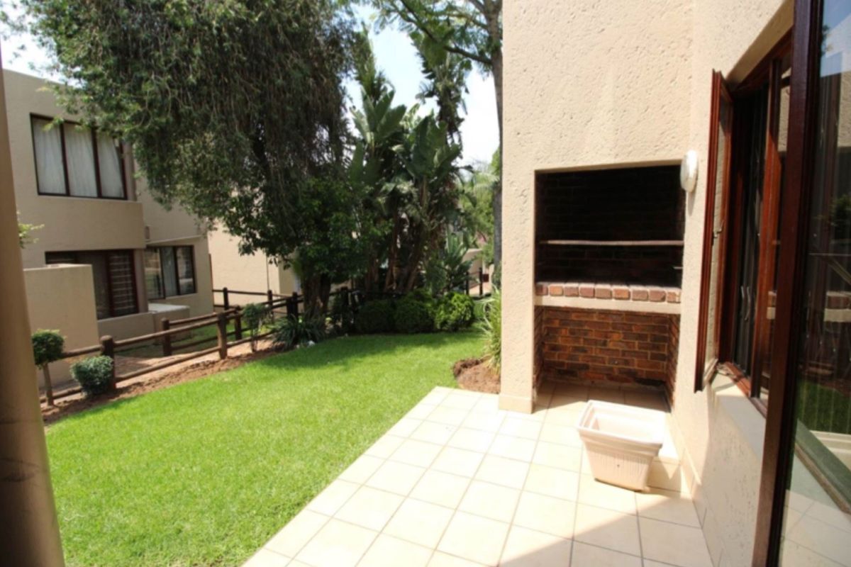 A private rear garden featuring a paved patio area with a built-in brick braai, overlooking a small lawn and established trees.