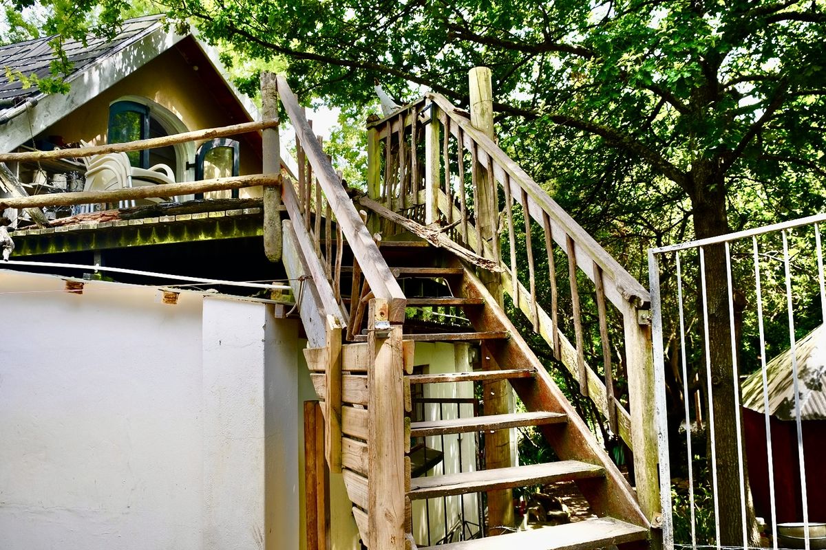 Exterior view of a rear property area featuring a weathered wooden staircase leading to an elevated deck with visible signs of wear.