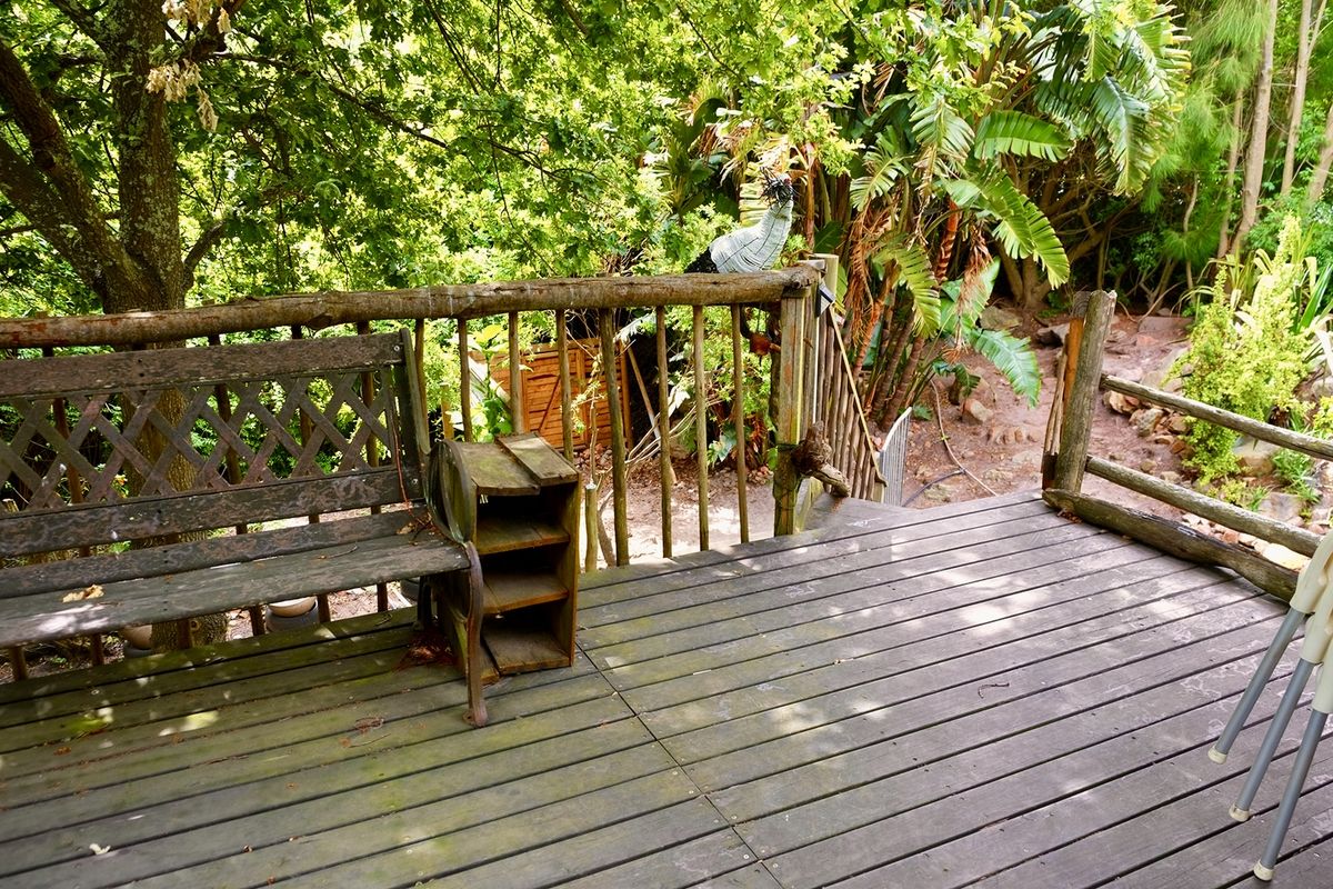 A rustic timber deck area featuring natural wood railings, overlooking a lush, tree-filled garden setting.