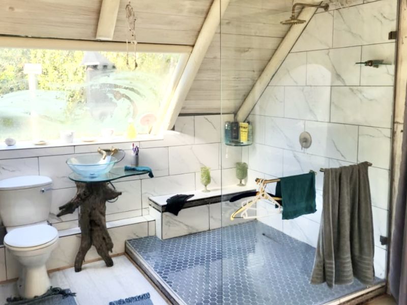 Unique attic bathroom featuring a glass vessel sink, walk-in shower with marble-look tiling, hexagonal floor tiles, and a large skylight window.