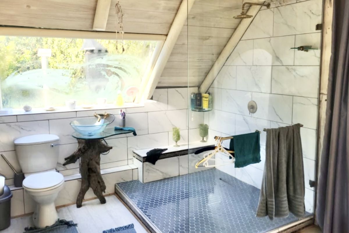 Unique attic bathroom featuring a glass vessel sink, walk-in shower with marble-look tiling, hexagonal floor tiles, and a large skylight window.