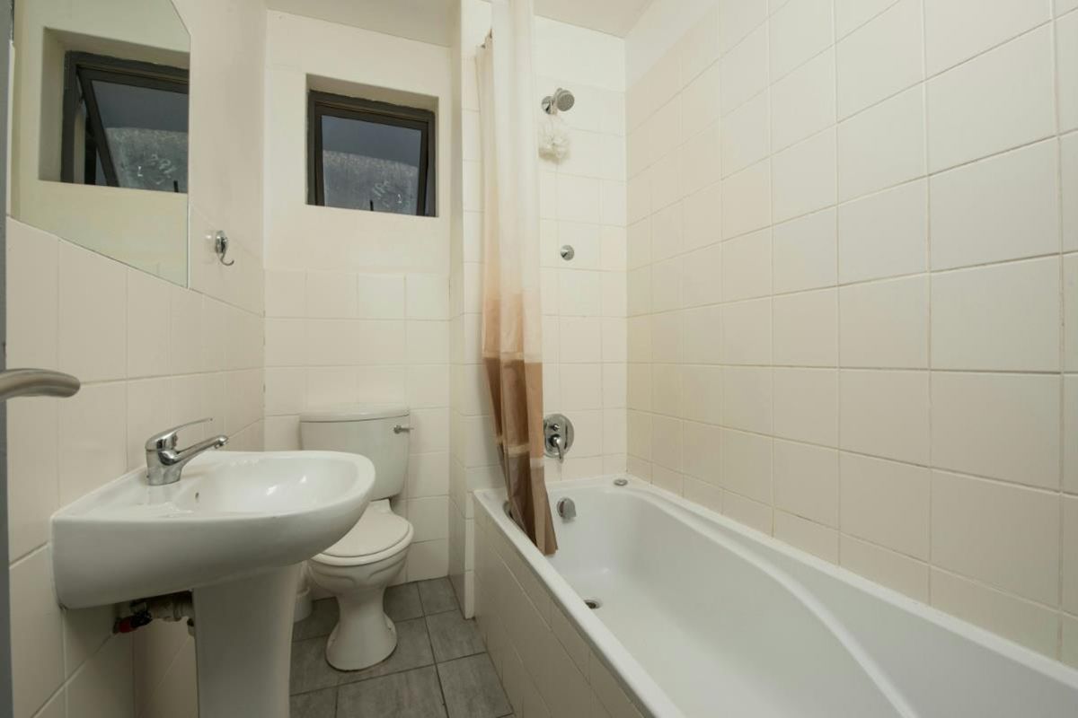 A functional bathroom featuring a pedestal sink, toilet, and a shower-over-bath combination with white wall tiling.