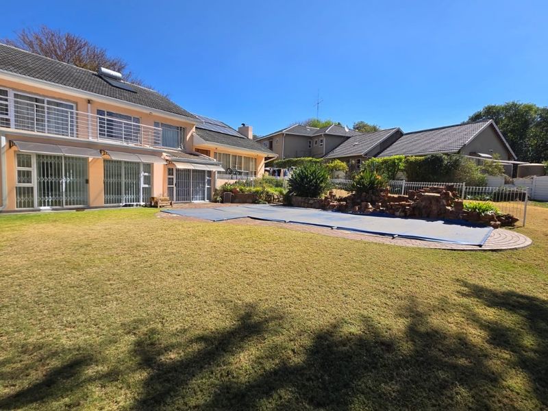 Rear view of the cottage featuring a spacious lawn, swimming pool with cover, and a multi-level exterior with balcony and security features.