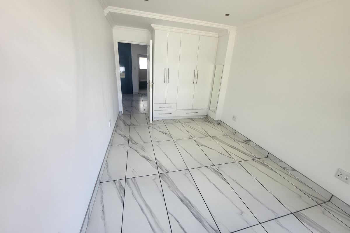 A bright, empty bedroom featuring modern marble-look floor tiles, recessed ceiling lighting, and built-in white cabinetry.