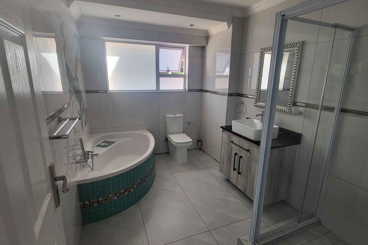 Modern bathroom featuring a corner bathtub with mosaic tiling, a glass-enclosed shower, a vanity with a vessel sink, and a toilet.
