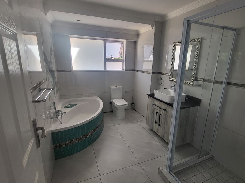 Modern bathroom featuring a corner bathtub with mosaic tiling, a glass-enclosed shower, a vanity with a vessel sink, and a toilet.