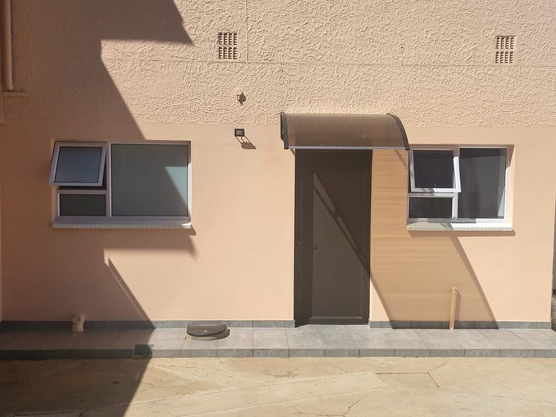 Exterior view of a cottage entrance featuring a modern door with a protective awning, tiled threshold, and aluminium-framed windows.