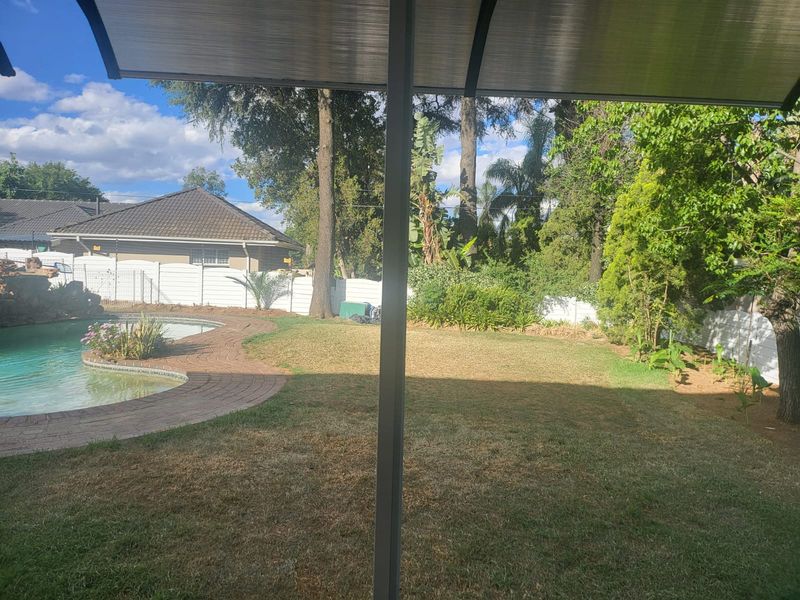 A view of the rear garden featuring a swimming pool with brick paving, surrounded by established trees and perimeter fencing.