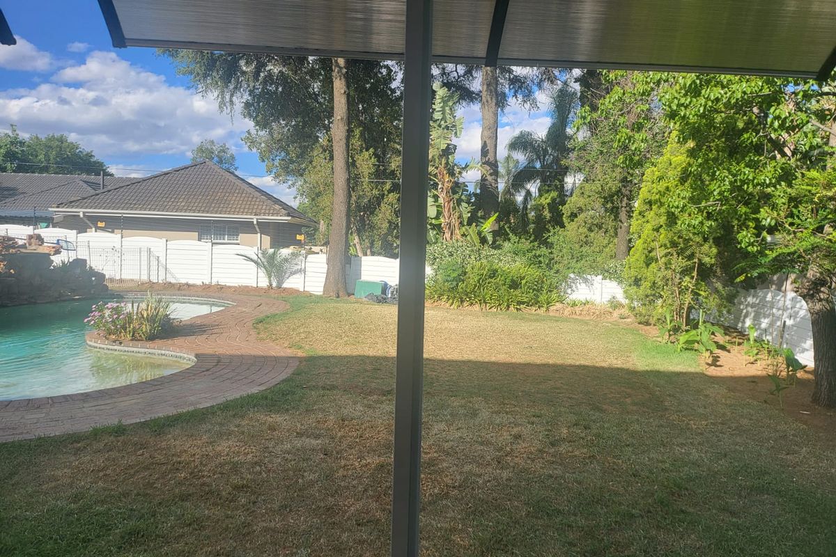 A view of the rear garden featuring a swimming pool with brick paving, surrounded by established trees and perimeter fencing.