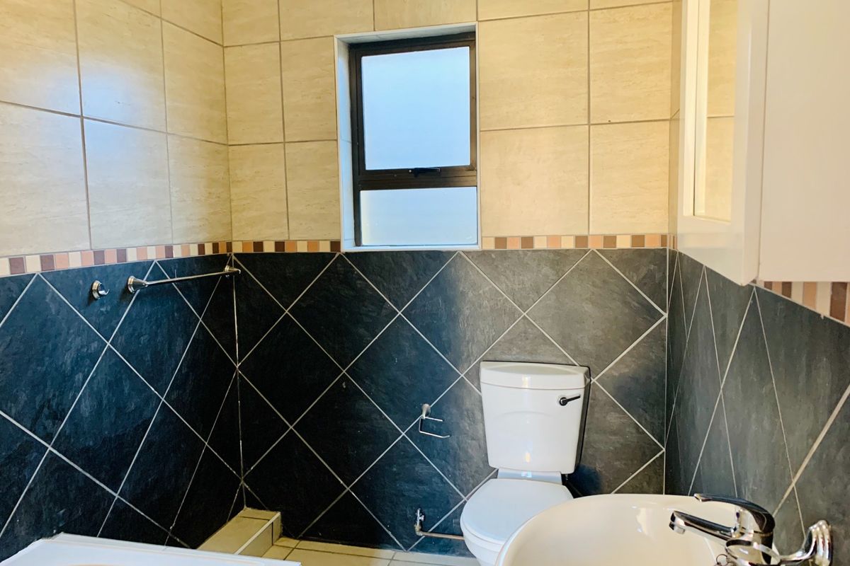 A functional bathroom featuring a toilet, basin with chrome mixer tap, and tiled walls with a decorative border.