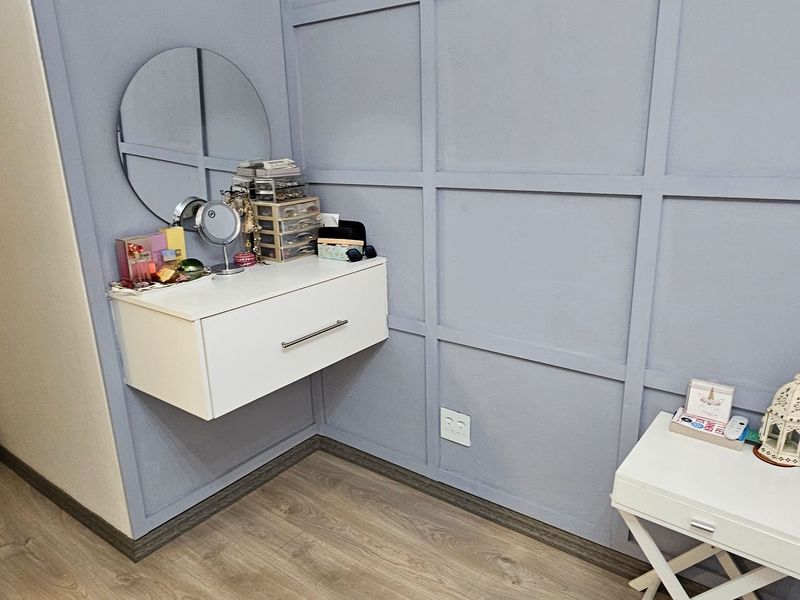 A bedroom corner featuring decorative wall paneling, light wood-look laminate flooring, and a modern wall-mounted floating drawer unit.