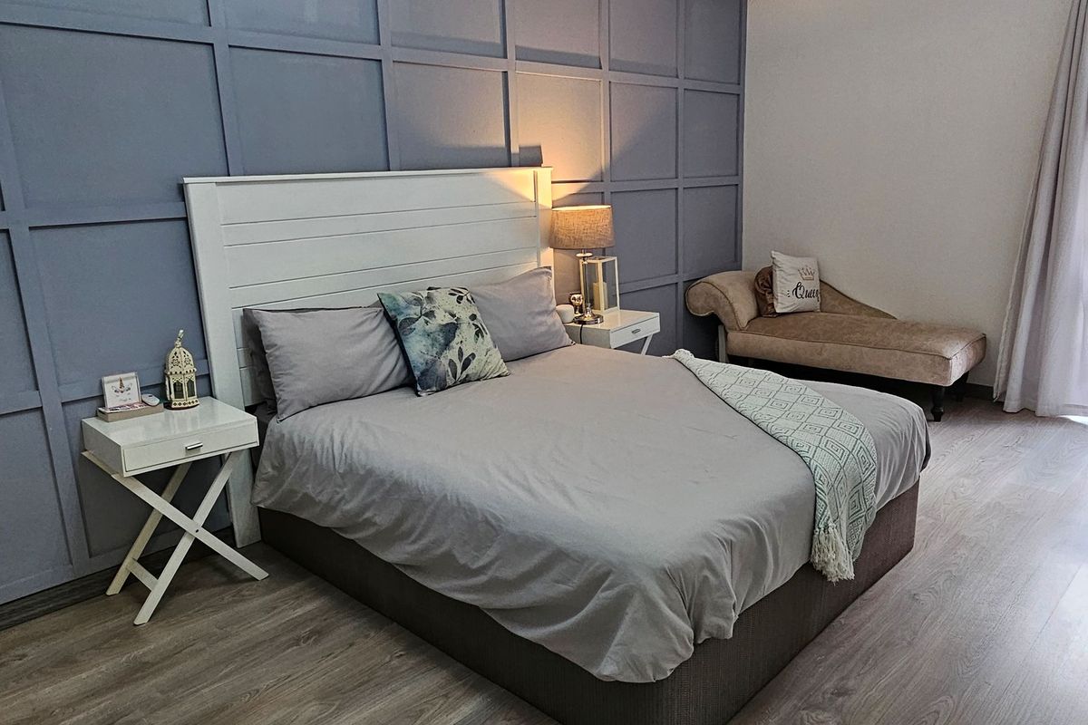 A well-maintained bedroom featuring modern laminate flooring and a decorative blue paneled feature wall, creating a contemporary and comfortable living space.
