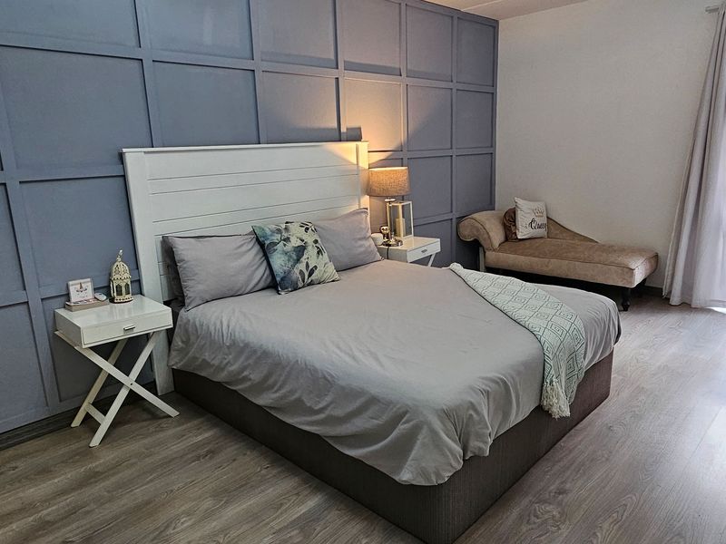 A well-maintained bedroom featuring modern laminate flooring and a decorative blue paneled feature wall, creating a contemporary and comfortable living space.