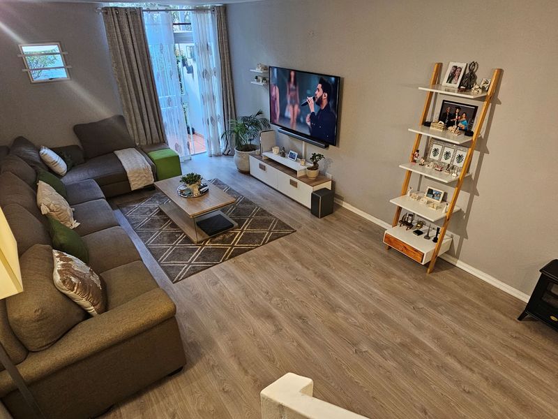 A well-maintained living room featuring modern laminate flooring, neutral wall tones, and a sliding glass door providing access to an outdoor area.