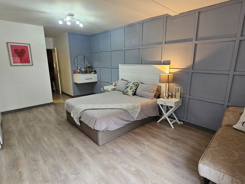 Spacious bedroom featuring modern laminate flooring, decorative wainscoting wall paneling, and a convenient built-in wardrobe with a floating vanity area.
