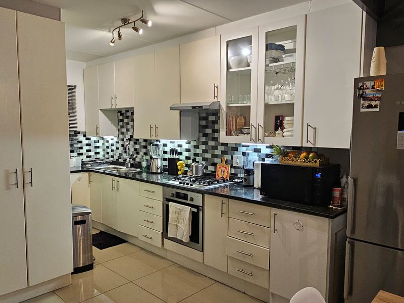 A well-appointed kitchen featuring white cabinetry, granite countertops, a mosaic tile backsplash, and integrated stainless steel appliances including an oven and gas hob.