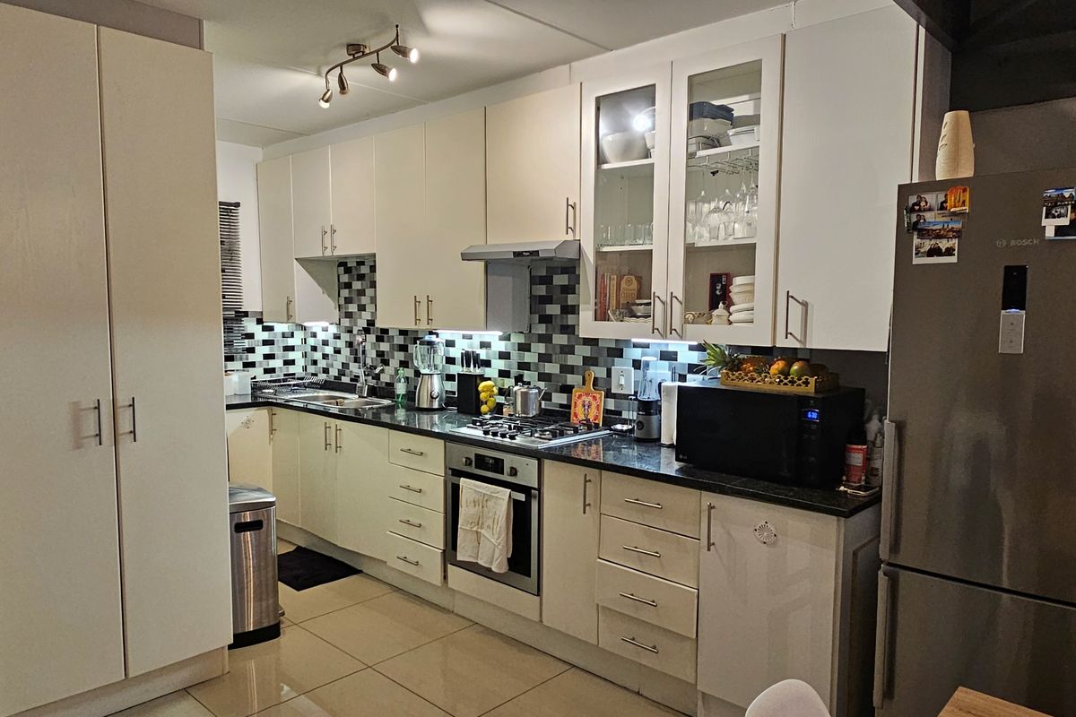 A well-appointed kitchen featuring white cabinetry, granite countertops, a mosaic tile backsplash, and integrated stainless steel appliances including an oven and gas hob.