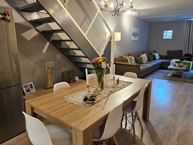 An open-plan living and dining area featuring laminate flooring, a central staircase with a modern railing, and a decorative chandelier.