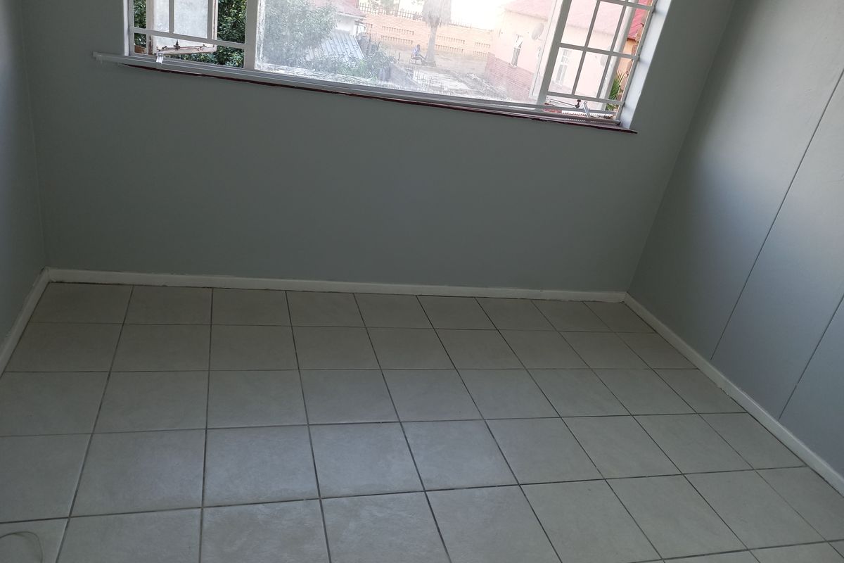 An empty bedroom featuring neutral grey walls and light-colored floor tiles, providing a clean and versatile space ready for personalization.