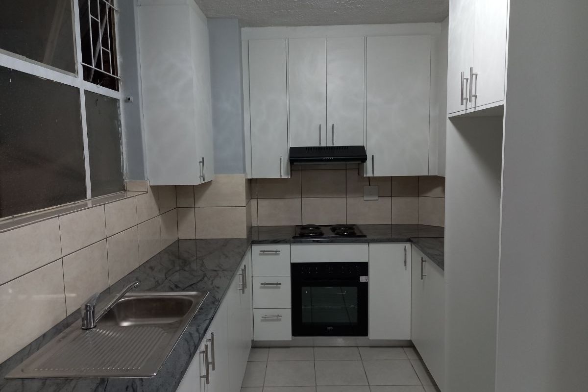 A compact, functional kitchen featuring white cabinetry, dark stone-look countertops, built-in oven, hob, and extractor fan with tiled backsplash and flooring.