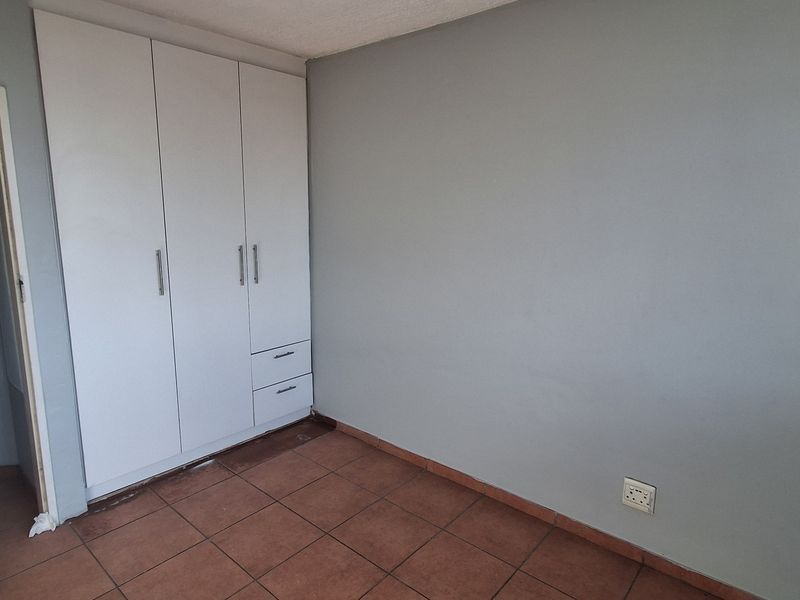 An empty bedroom featuring built-in cupboards, tiled flooring, and neutral wall paint, offering a blank canvas for personalization.