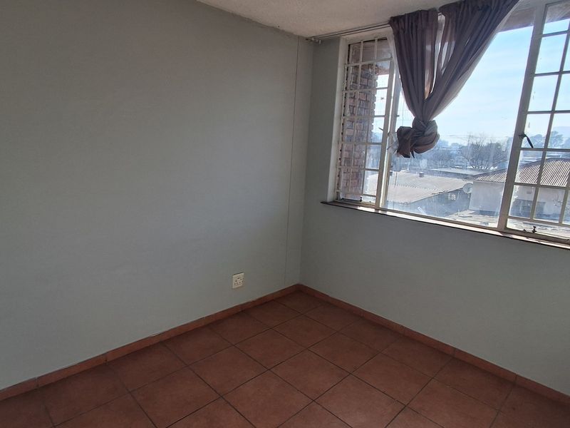 An empty bedroom featuring tiled flooring, a large window with security bars, and neutral wall paint, offering a blank canvas for personalization.