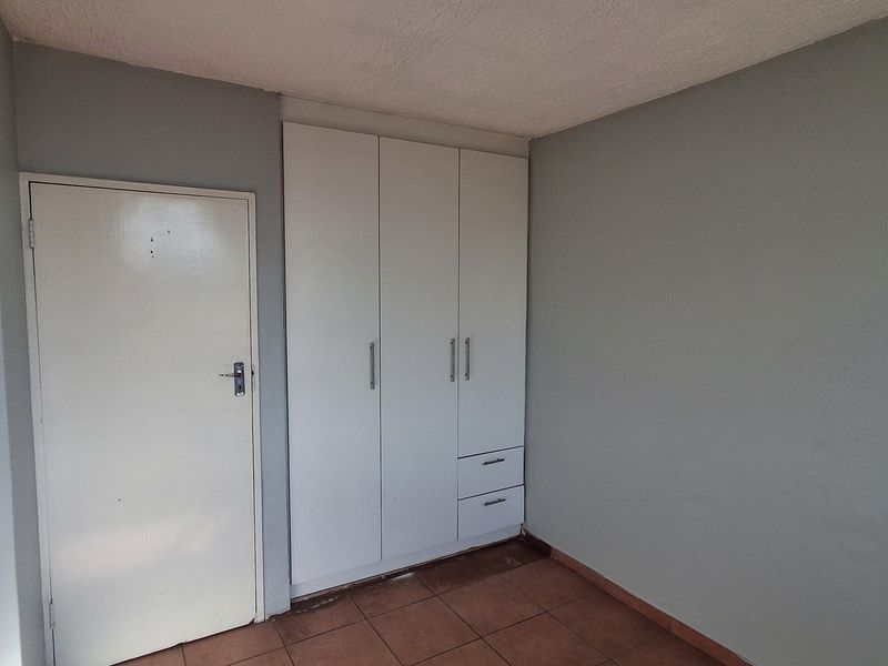 A simple bedroom featuring neutral grey walls, tiled flooring, and a white built-in wardrobe with integrated drawers.
