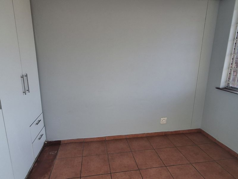 An empty bedroom featuring built-in cupboards, tiled flooring, and a window fitted with security bars.
