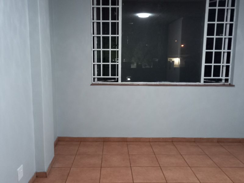 An empty bedroom featuring tiled flooring and a window fitted with security bars.
