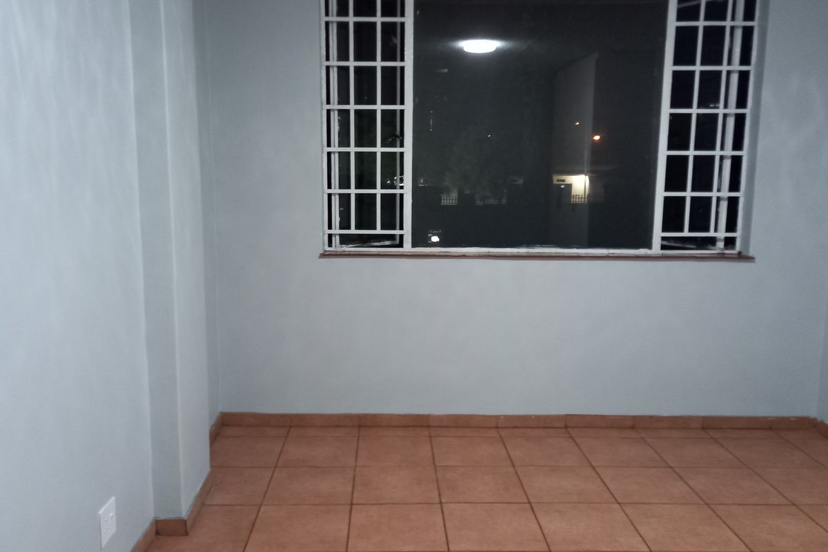 An empty bedroom featuring tiled flooring and a window fitted with security bars.