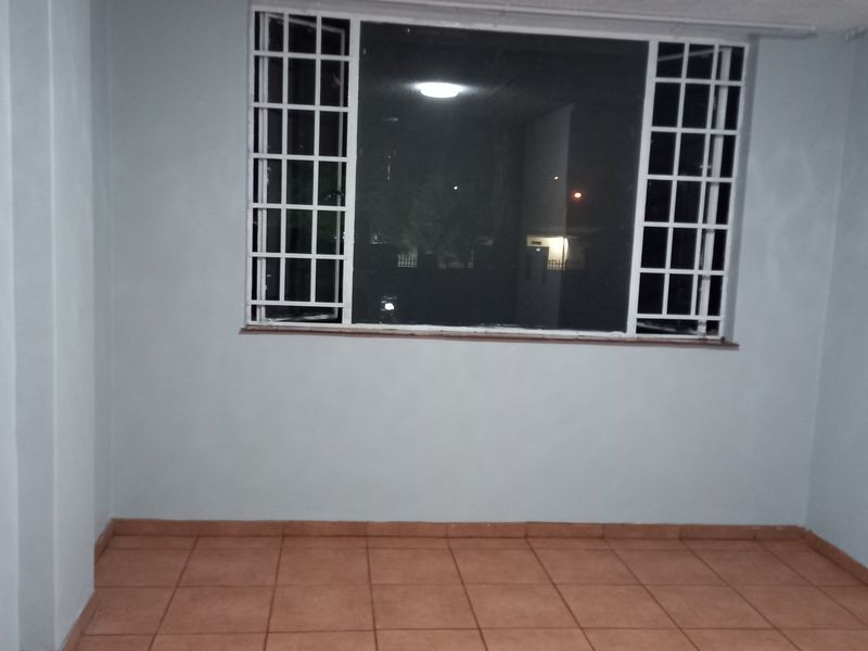 An empty living room featuring tiled flooring and a window fitted with security bars.