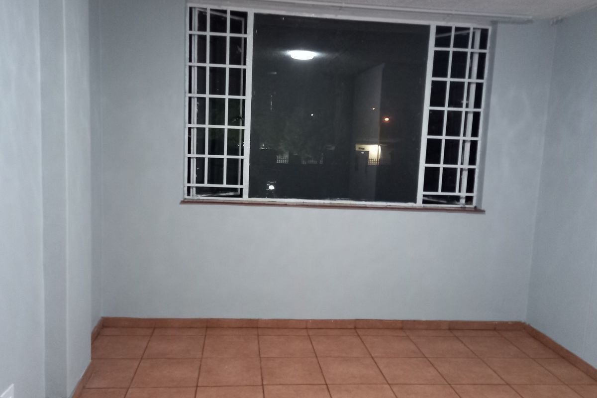 An empty living room featuring tiled flooring and a window fitted with security bars.