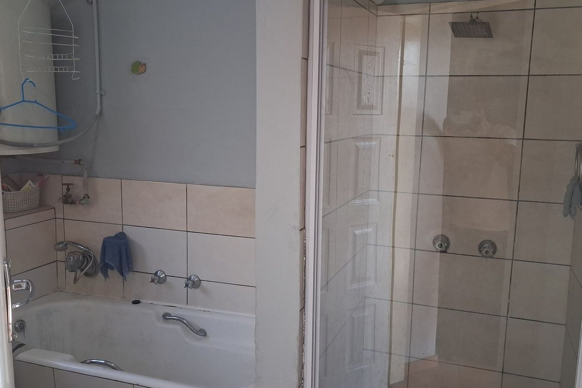 A functional bathroom featuring a separate bathtub and glass-enclosed shower with tiled walls and standard chrome fixtures.