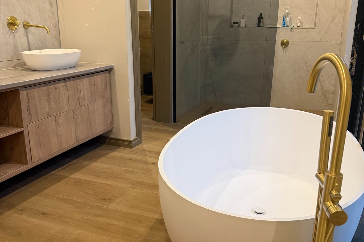 Modern bathroom featuring a freestanding bathtub, wall-mounted gold faucet, floating vanity with stone countertop, and a walk-in shower with built-in niche.
