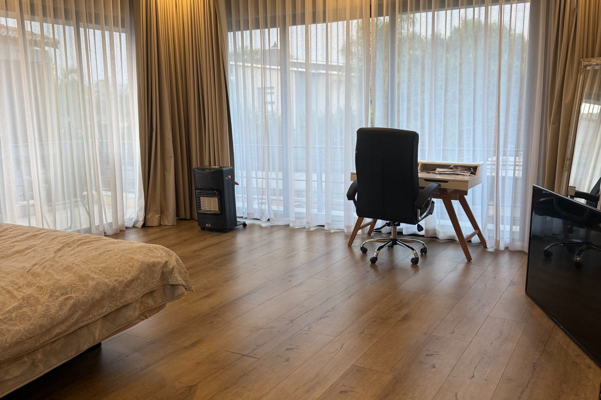 Spacious bedroom featuring wood-look laminate flooring, recessed ceiling lighting with warm cove accents, and floor-to-ceiling curtains covering large sliding glass doors.