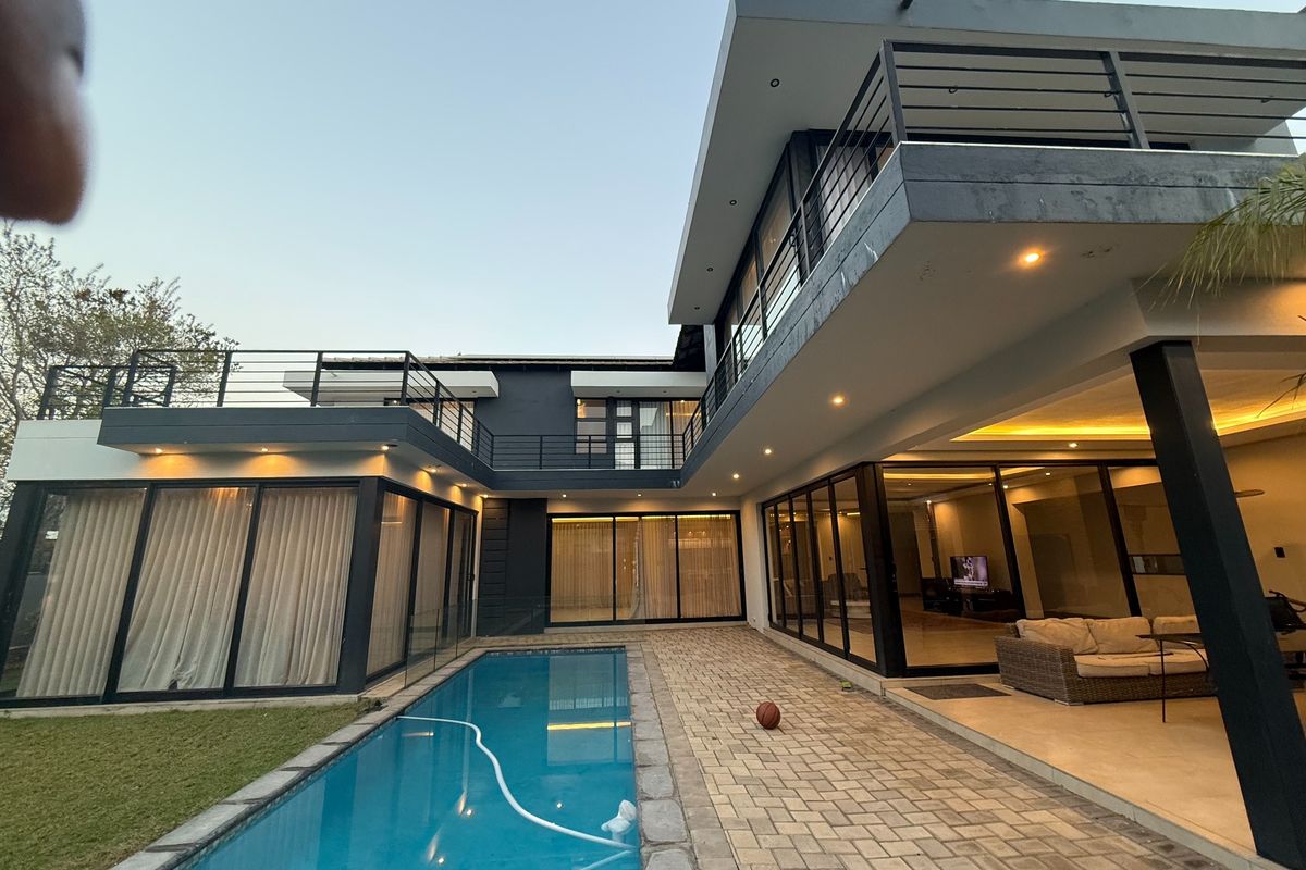 Modern double-story residence featuring a swimming pool, paved patio area, and extensive glass sliding doors connecting indoor and outdoor living spaces.