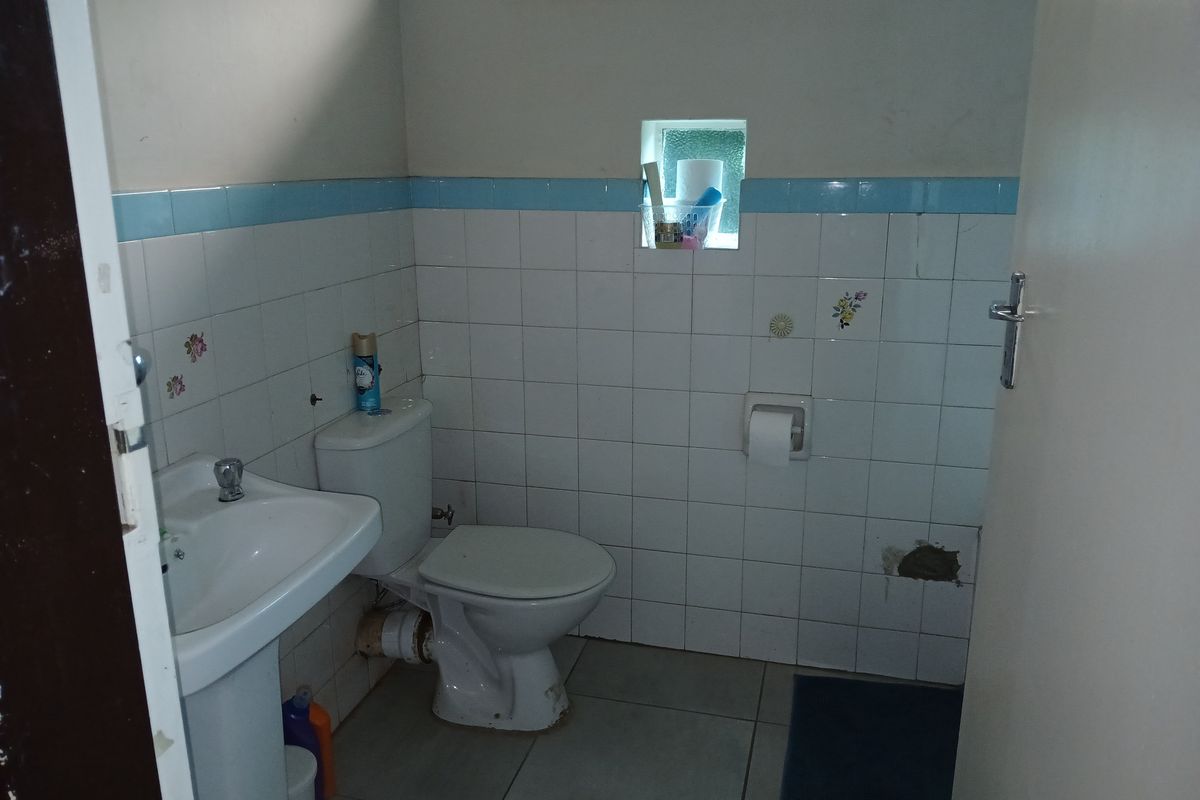 A compact bathroom featuring a pedestal basin, toilet, and tiled finishes, currently showing signs of wear and minor wall damage.