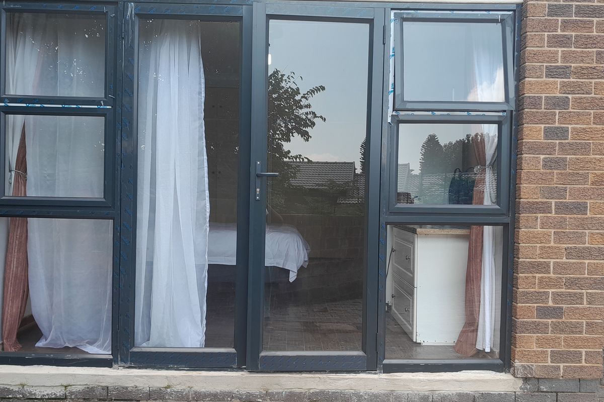 Exterior view of a rear facade featuring modern dark aluminium framed glass doors and windows set into a brick wall.