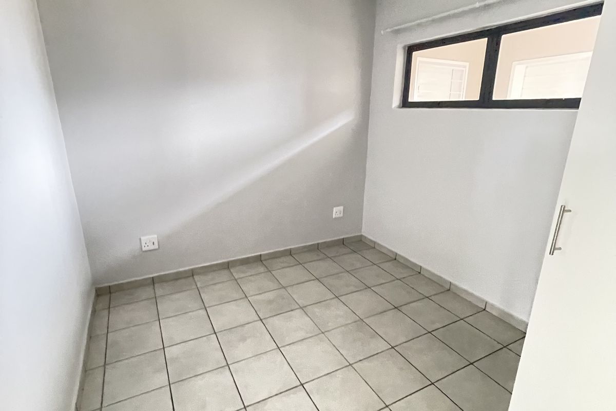 A clean, empty bedroom featuring neutral tiled flooring, a built-in cupboard, and a high-set window providing natural light.