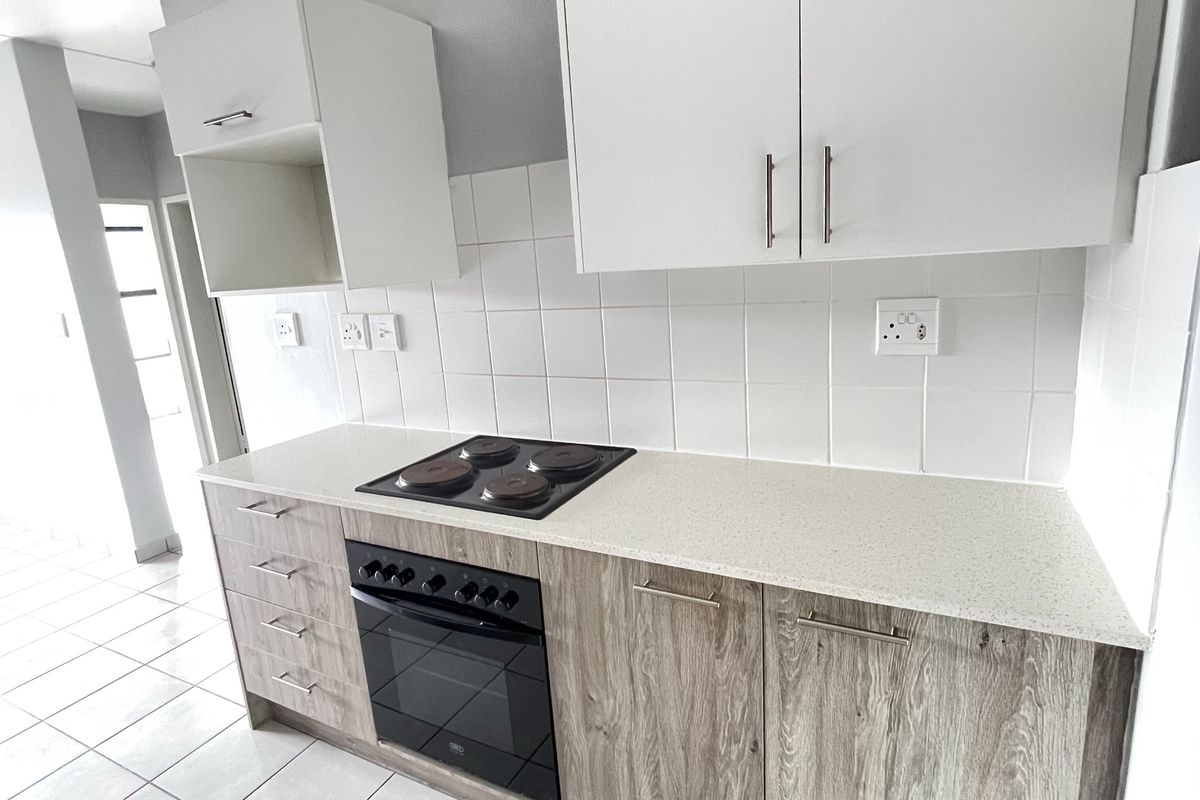 A clean, modern kitchen featuring wood-grain lower cabinetry, white upper cabinets, a stone-look countertop, and a built-in electric oven and hob.
