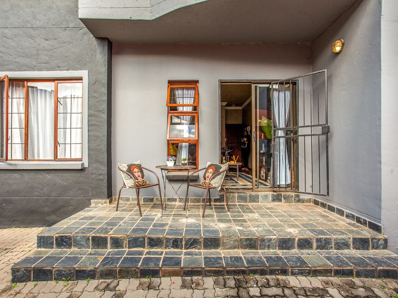 A ground-level patio area featuring dark tiled flooring, a security gate entrance, and exterior wall lighting, providing a functional outdoor transition space.