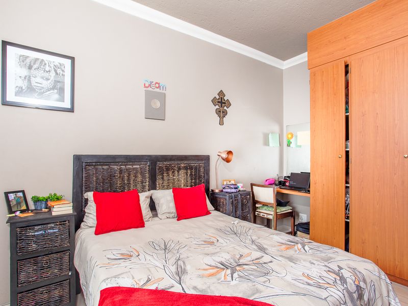 A functional bedroom featuring a built-in wooden wardrobe and decorative ceiling coving, providing practical storage and a neutral base for interior design.