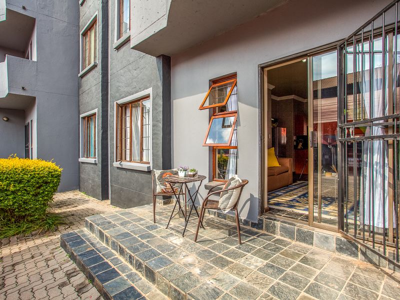 A ground-floor patio featuring slate tile flooring, a sliding glass door with security gate, and access to a paved walkway and garden area.