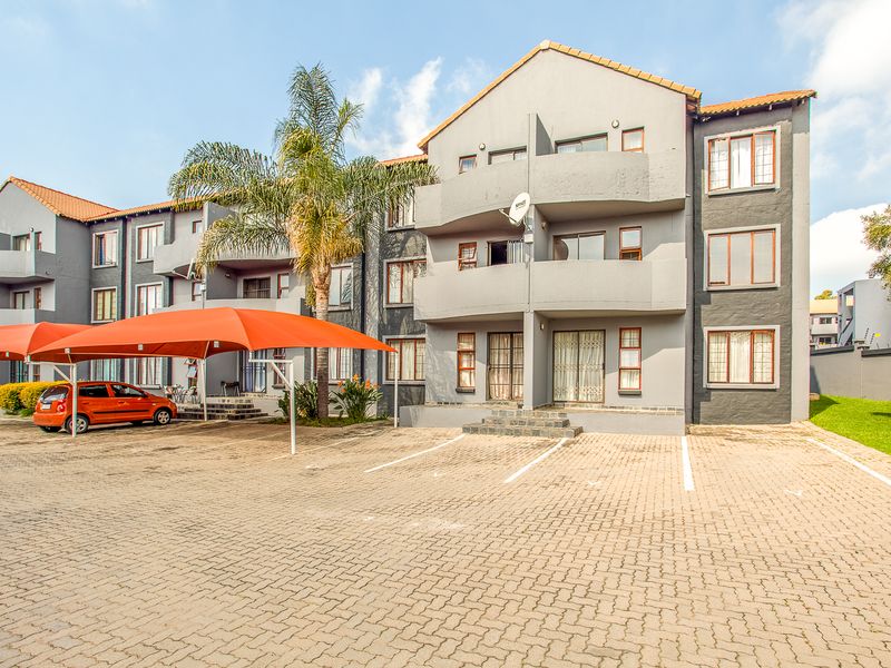 Front elevation of a multi-story apartment complex featuring paved parking, covered carports, and private balconies for each unit.