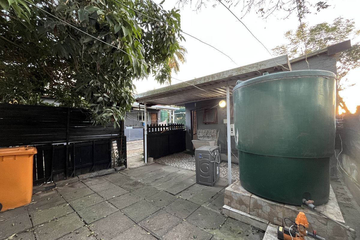 Rear exterior area featuring a covered patio, paved flooring, a large water storage tank, and a utility sink.