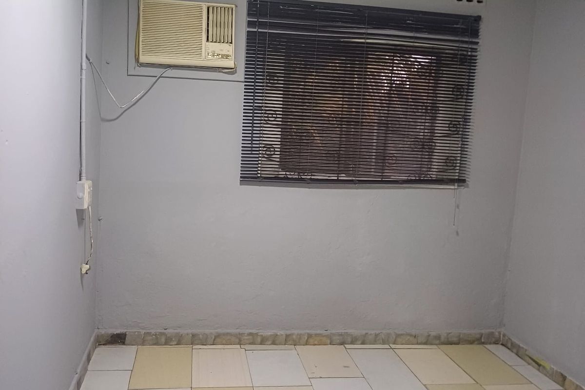 An empty bedroom featuring tiled flooring, a window with fitted blinds, and a wall-mounted air conditioning unit.