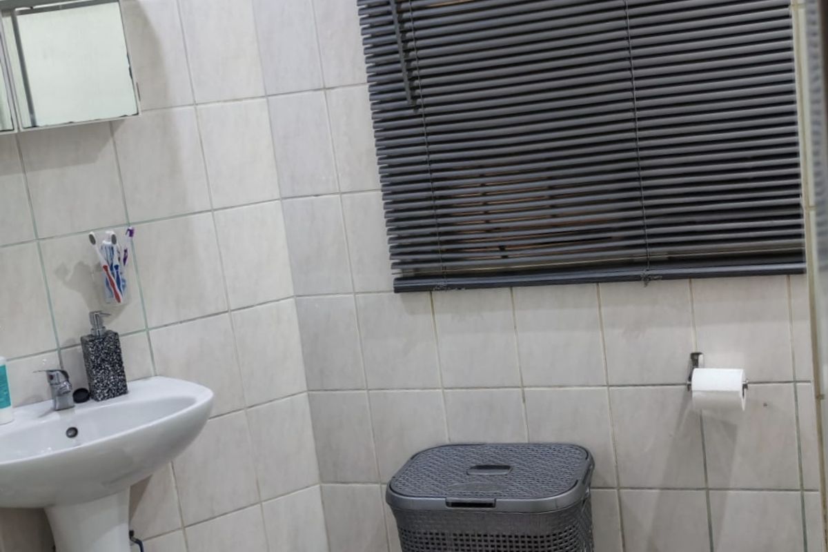 A functional bathroom featuring a pedestal basin, tiled walls and flooring, and venetian blinds for privacy.