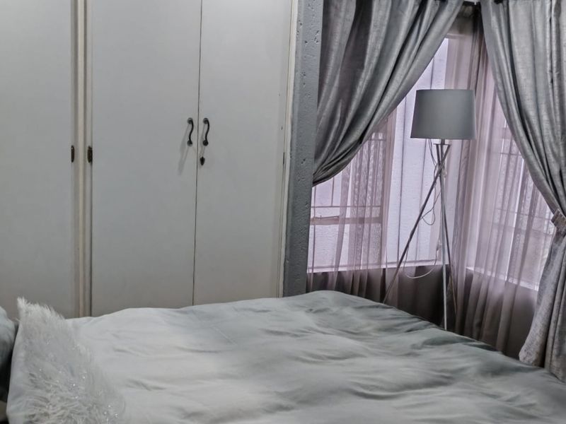 A cozy bedroom featuring built-in cupboards, recessed downlighting, and a corner window arrangement.